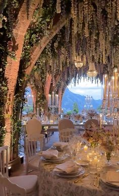 an outdoor dining area with tables, chairs and chandeliers decorated with flowers and greenery