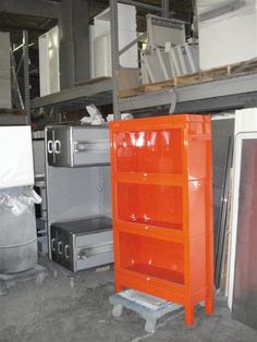 an orange shelf sitting in the middle of a room next to other metal appliances and cabinets