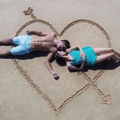 two people laying in the sand next to a heart