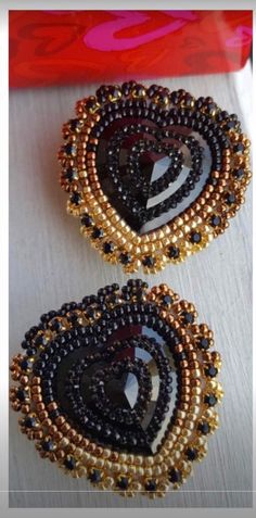 two black and gold beaded brooches sitting on top of a white table