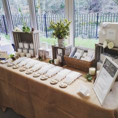 the table is set up with candles, pictures and other items for sale in front of large windows