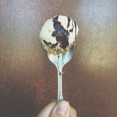 a person holding a spoon with some kind of dessert on it's side, in front of a wooden table