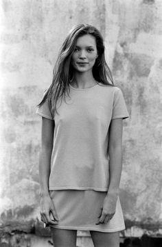 a woman standing in front of a wall wearing a short skirt and t - shirt