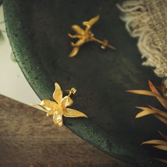 two gold flower earrings sitting on top of a green tray next to some plants and lace