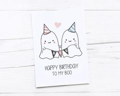 a birthday card with two white cats wearing party hats and bow ties, on top of a wooden table