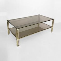 a glass and brass coffee table with two shelves on each side, against a white background