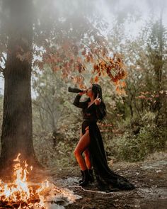 a woman dressed in black standing next to a fire and looking into the distance with her hands on her hips