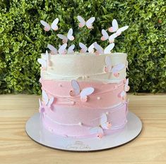 there is a three layer cake with butterflies on the top and pink frosting around the edges