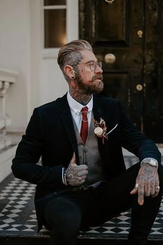 a tattooed man in a suit sitting on a black and white checkered floor