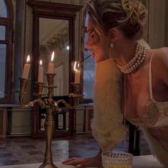 a woman in white dress leaning over a table with a candle holder on top of it