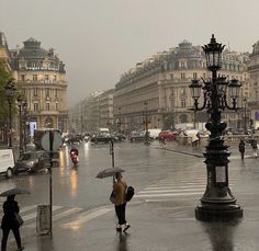 people walking in the rain with umbrellas on a city street near many old buildings