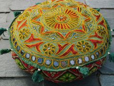 a decorative round pillow with tassels and beads on the top sitting on a stone floor