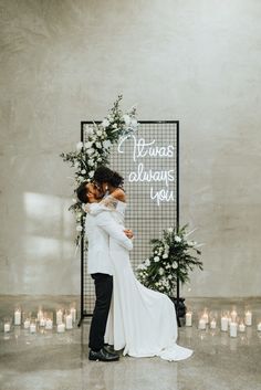 a newly married couple kissing in front of a wedding sign with candles and greenery