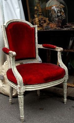 an old chair with red velvet upholstered on the back and arms, sitting in front of a mirror