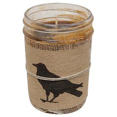 a candle with a bird on it sitting in front of a glass jar filled with sand