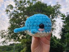 a hand holding up a small crocheted blue and white animal with black eyes