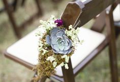 an arrangement of flowers and succulents is placed on the back of a wooden chair