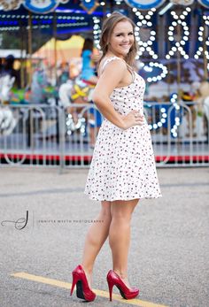 a woman in a white dress and red high heels posing for the camera at an amusement park