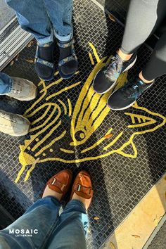 three people standing in front of a yellow fish design on the ground with their feet up