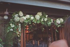 a woman standing in front of a restaurant with flowers on the door and tables outside