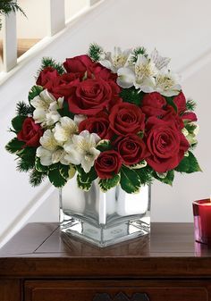 a bouquet of red roses and white flowers in a square glass vase on a table