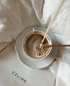 a white plate topped with a cup of coffee next to a napkin and paper on top of it