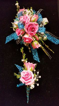 two pink and blue flowers are placed on a black surface with ribbons around them,