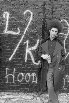 a man standing next to a brick wall with graffiti on it