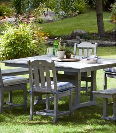 an outdoor table with chairs and a potted plant on it in the middle of some grass