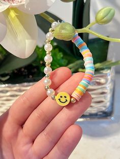 a hand holding a beaded bracelet with a smiley face on it