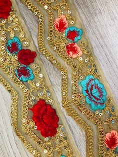 two pieces of gold and red beaded fabric with flowers on it, sitting on a wooden surface