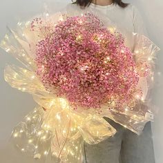 a woman holding a bouquet of pink flowers with fairy lights on it's side