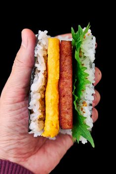 a hand holding a half eaten sandwich in it's left hand, with rice and lettuce on the side