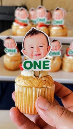 a person holding up a cupcake with an image of a baby's face on it