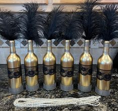 six wine bottles with black lace on them and some feathers in the middle are lined up next to each other