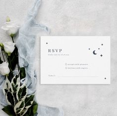 a white wedding card with flowers and greenery next to it on a blue cloth