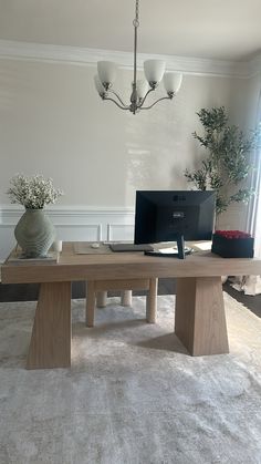 a desk with a computer on it in front of a window and a vase filled with flowers