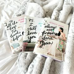 three books sitting on top of a bed covered in white sheets and blankets next to each other