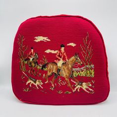 a red purse with an embroidered horse and rider design on the front, featuring two men riding horses