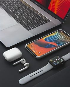 an apple watch, ear buds, and iphone on a desk next to a laptop