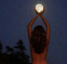 a woman holding up a white ball in the air at night with trees behind her