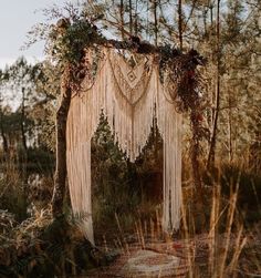 an outdoor wedding ceremony with macrami and greenery draped over the altar, surrounded by tall grass