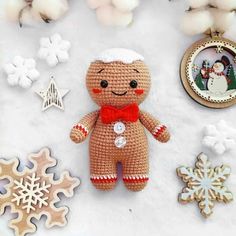 a crocheted teddy bear sitting on top of snow covered ground next to christmas decorations