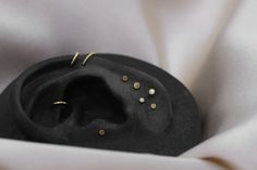 a black hat with gold studs on it's side sitting on a white cloth