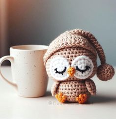 a crocheted owl sitting next to a coffee cup