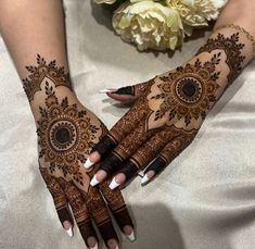 two hands with henna designs on them, one is holding a bouquet of flowers