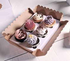 a box filled with cupcakes sitting on top of a white table next to a vase