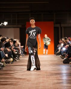 a model walks down the runway in a black t - shirt and pants with white lettering on it