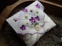 a white pillow with purple flowers on it and a button in the center is sitting on some dried grass