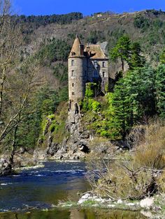 an old castle sitting on the side of a mountain next to a river in front of it